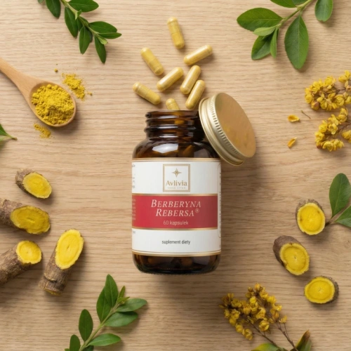Berberyna Rebersa Avlivia - otwarty słoiczek z kapsułkami na jasnym drewnianym tle, obok korzenie berberysu o żółtym przekroju, proszek berberyny na drewnianej łyżeczce i żółte kwiaty berberysu